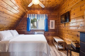 A cozy room with a bed, a bench, a TV, and a window with curtains. - Juniper Presents: Chalet #76 3BR Chalet Nr Beach & Resort Amenities (Stevensville)