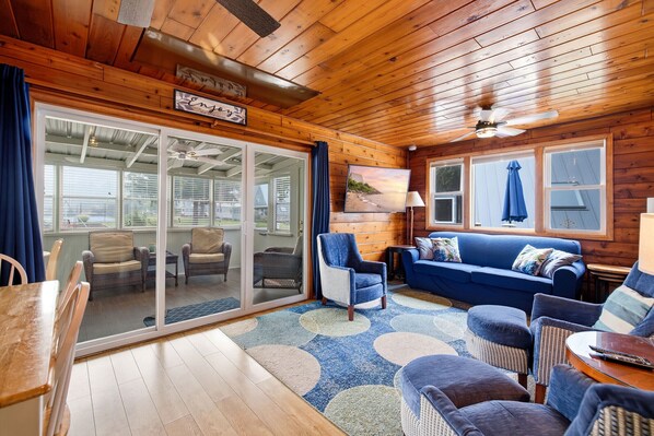A cozy cabin interior with a wooden ceiling, a blue sofa, and a dining area with a table and chairs. - Juniper Presents: Chalet #76 3BR Chalet Nr Beach & Resort Amenities (Stevensville)