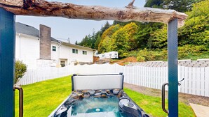 Ein Whirlpool mit Holzbeschattung, ein weißes Haus und ein eingezäunter Garten.