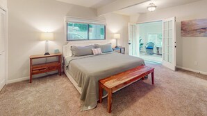 Ein Schlafzimmer mit einem Bett, Nachttischen, einer Bank und einer Tür, die auf einen Balkon führt.