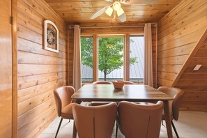 Un intérieur en bois comprenant une table à manger, des chaises, un ventilateur de plafond et une fenêtre donnant sur des arbres.