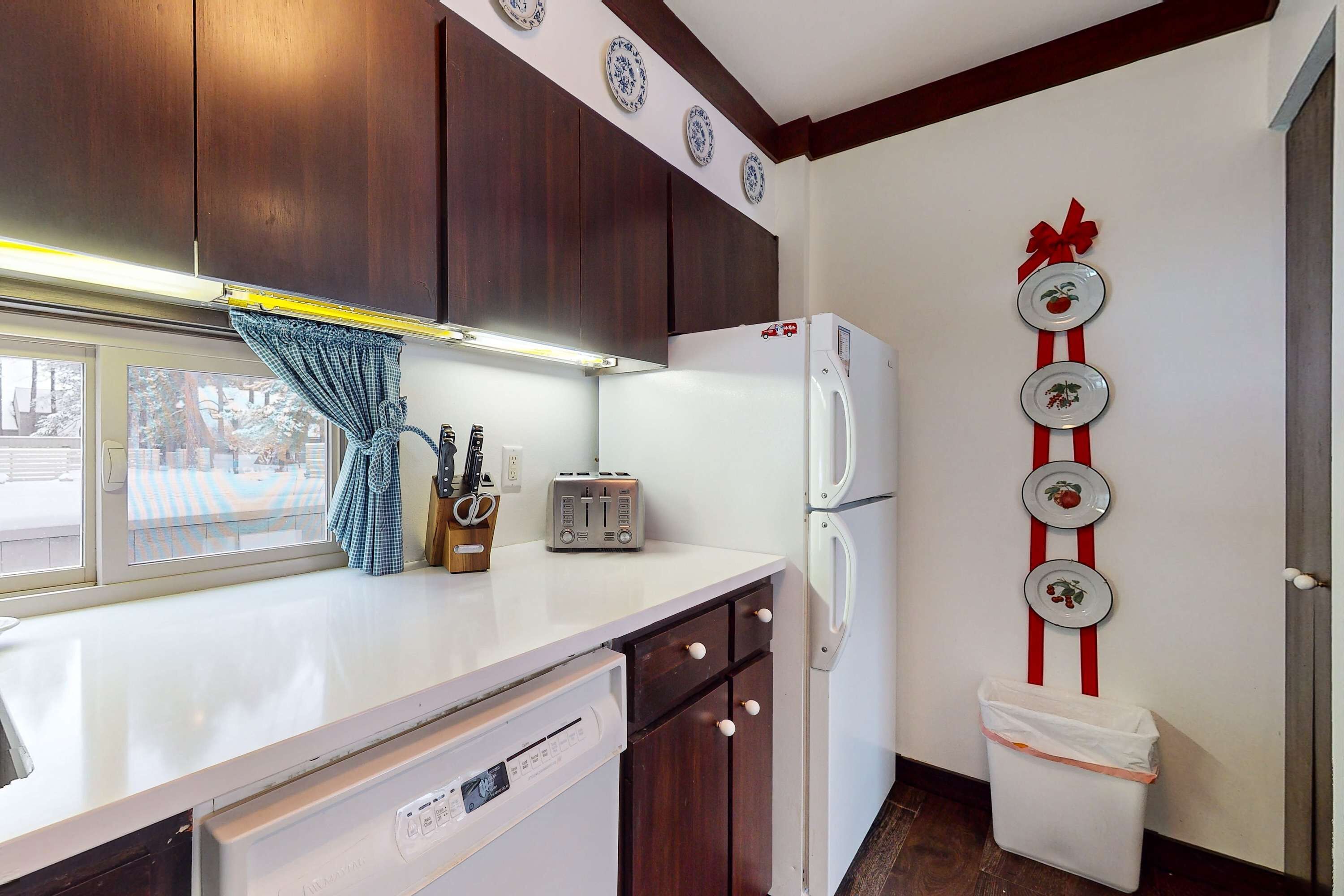 A kitchen with wooden cabinets, a white countertop, a toaster, a refrigerator, and a trash bin.