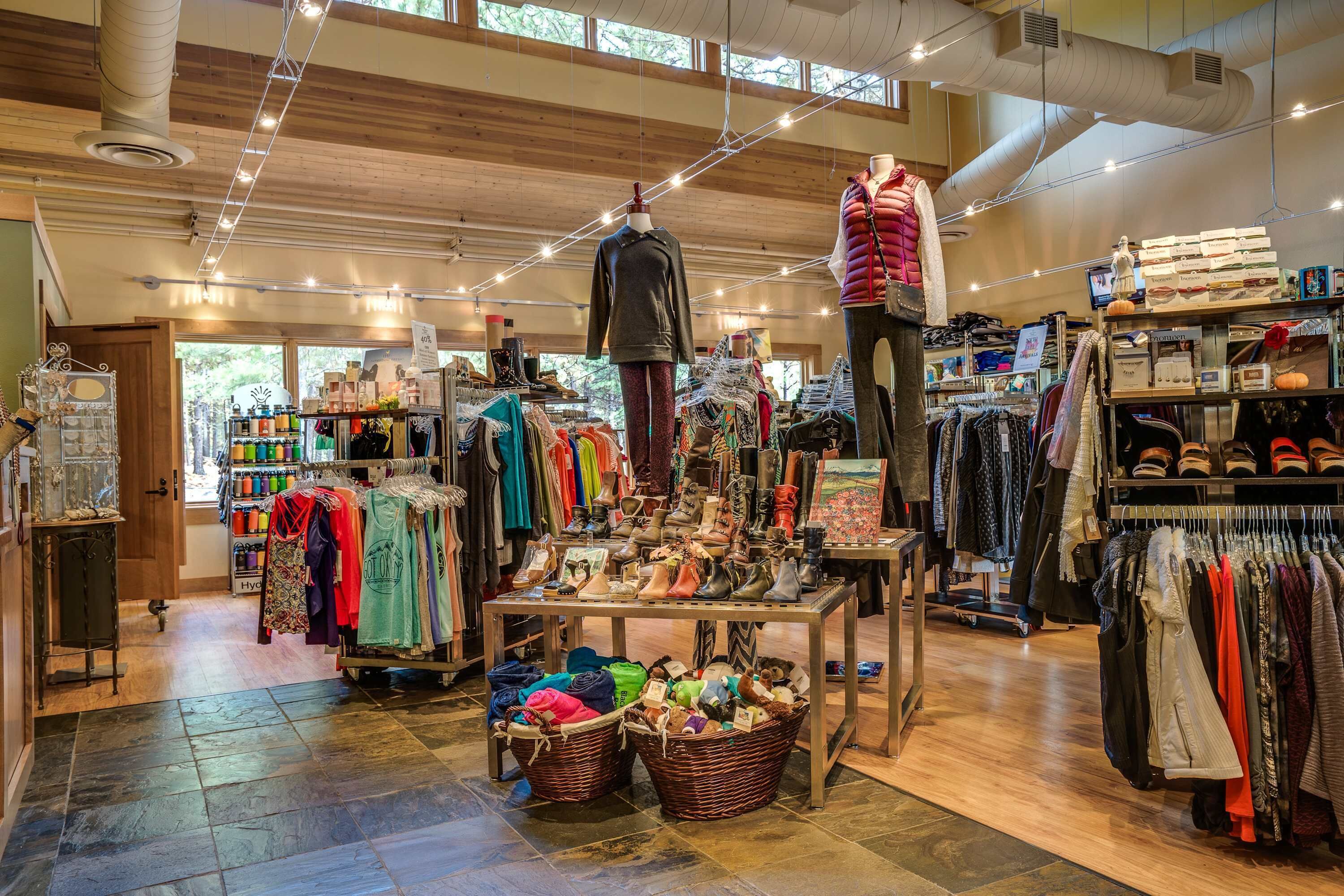A clothing store with racks of clothes, a mannequin, and a table with shoes.