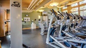 Un gimnasio con equipo de ejercicio, techo de madera y ventanas amplias.