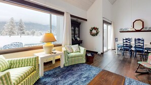 Una sala de estar acogedora con vista a un paisaje nevado, una chimenea, un comedor con sillas azules y una estantería.