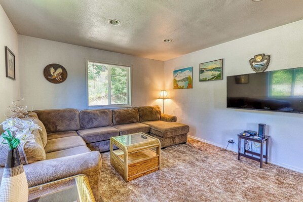 A living room with a sectional sofa, a glass coffee table, a lamp, and artwork on the walls.