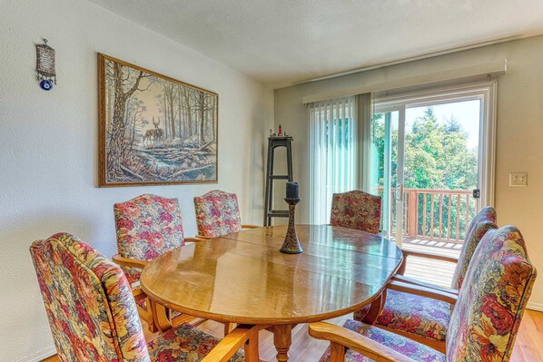 A dining area with a round wooden table, floral upholstered chairs, a painting on the wall, and a view through a sliding glass door. - Secluded & comfortable dog-friendly home with deck plus ATV & boat parking (North Bend)