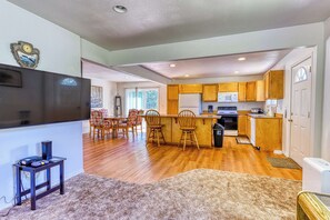 A modern kitchen with wooden cabinets, a microwave, and a refrigerator. There is a dining area with chairs and a table.