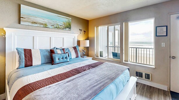 Un dormitorio con una cama grande, un cuadro sobre la cama, una ventana con vistas y un cartel en la pared.