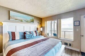 A bedroom with a large bed, a painting above the bed, a window with a view, and a sign on the wall.