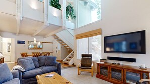 Een ruime woonkamer met een grote televisie, een bank, een salontafel, een fauteuil, en een trap die leidt naar een verdieping.