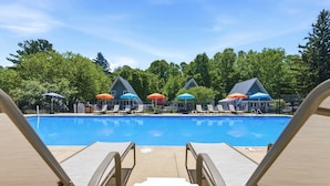 Une piscine entourée d’arbres et de bâtiments, avec des chaises longues et des parasols.