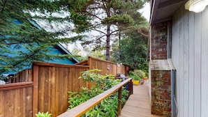 A wooden deck with a railing, surrounded by greenery and a brick wall. - Adorable dog-friendly home with gas grill, gas fireplace & private back patio (Manzanita)