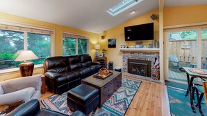 A living room with a fireplace, a ceiling fan, and a TV mounted on the wall. - Adorable dog-friendly home with gas grill, gas fireplace & private back patio (Manzanita)