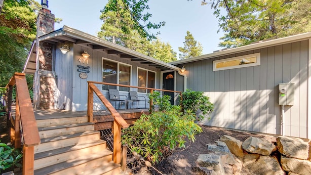 A wooden staircase leading to a covered deck with outdoor seating, a stone wall, and a chimney. - Adorable dog-friendly home with gas grill, gas fireplace & private back patio (Manzanita)