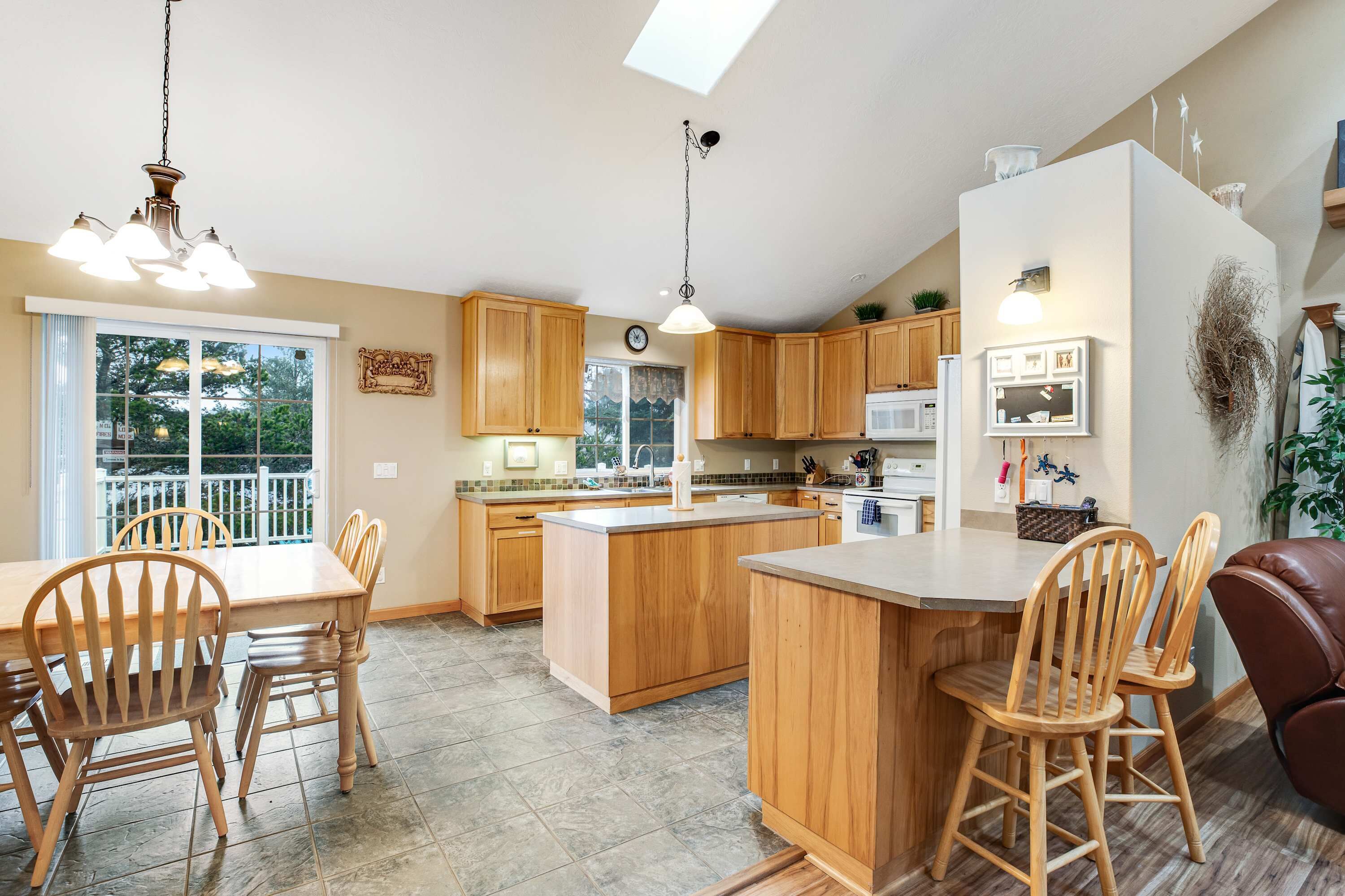 Une cuisine avec des meubles de rangement en bois, un îlot central, un coin repas avec des chaises et un luminaire au plafond.