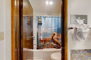 A bathroom with a shower curtain depicting a lighthouse, pelican, and houses. - Retro-chic beach room with fast WiFI - walk to Old Town shops & restaurants (Bandon)
