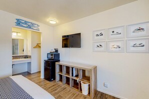 A room with a bed, a wooden console table, a TV, and framed pictures on the wall. - Retro-chic beach room with fast WiFI - walk to Old Town shops & restaurants (Bandon)