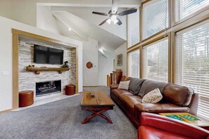A living room with a stone fireplace, a leather sofa, a wooden coffee table, and a ceiling fan.