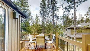 Um deck de madeira com mesa e cadeiras, cercado por um guarda-corpo de madeira, com vista para uma área arborizada.