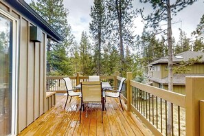 A wooden deck with a table and chairs, surrounded by a wooden railing, overlooking a forested area.
