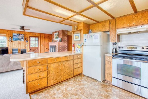 A kitchen with wooden cabinets, a refrigerator, a stove, and a brick fireplace. - Dog-Friendly Home with Ocean Views, Easy Beach and Bay Access, and Free WiFi (Waldport)