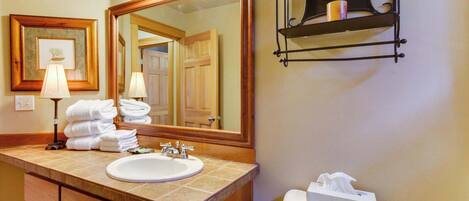 A bathroom with a sink, mirror, towel rack, and toilet paper holder.