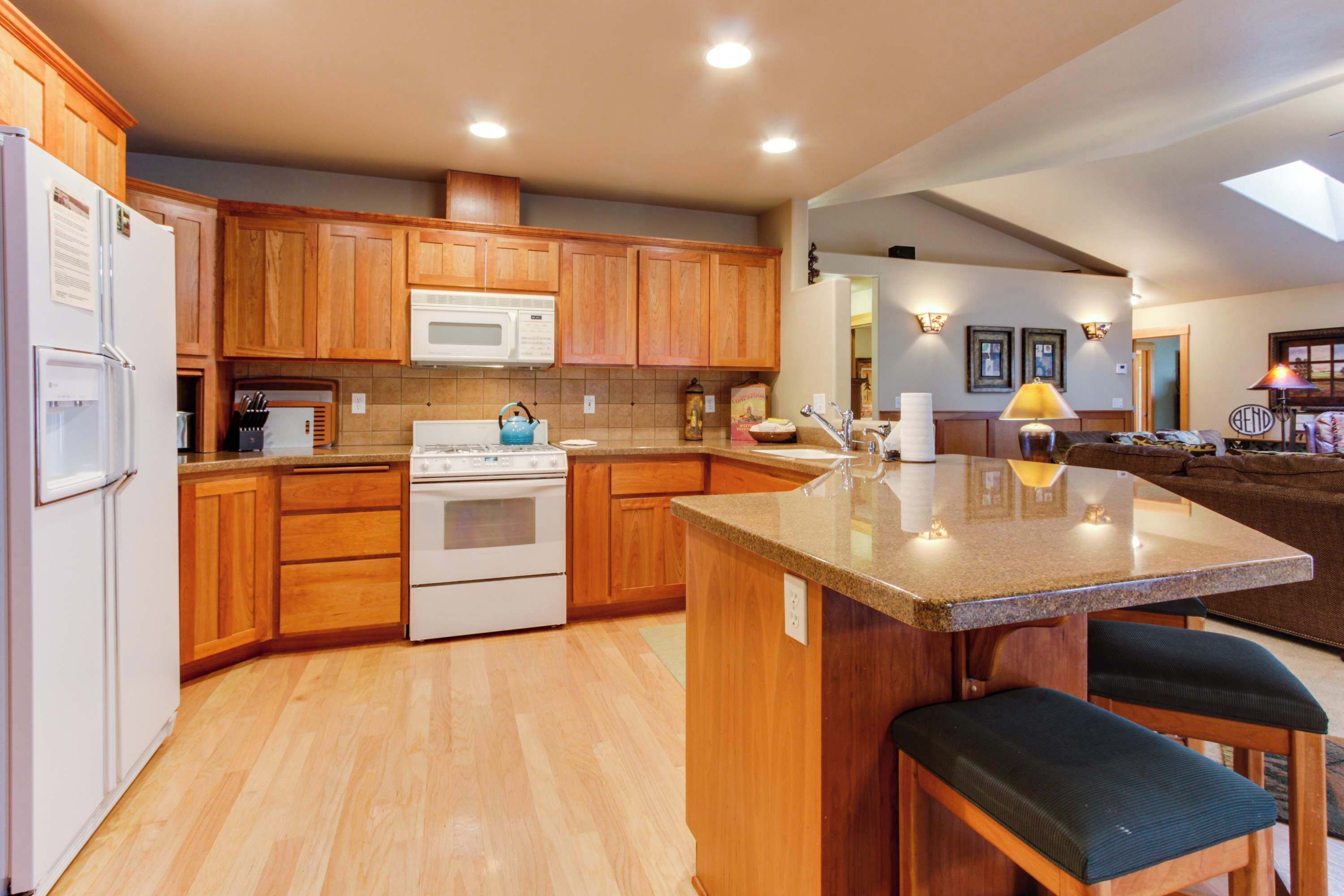 A kitchen with wooden cabinets, a microwave, stove, and a granite countertop island with bar stools.