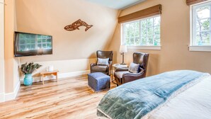 A bedroom with a bed, two chairs, a TV, a window, and a wall decoration. - Lovely studio guesthouse with ocean views, outdoor deck & washer/dryer (Warrenton)