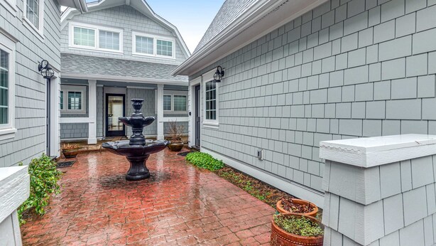 A courtyard with a brick pathway, a central fountain, and a house with grey siding and white trim. - Lovely studio guesthouse with ocean views, outdoor deck & washer/dryer (Warrenton)