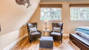 A room with two leather chairs, a small table with a lamp, a bed, and a window with blinds. - Lovely studio guesthouse with ocean views, outdoor deck & washer/dryer (Warrenton)