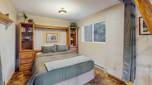 Un dormitorio con cama, estantería, ventana y ventilador de techo.