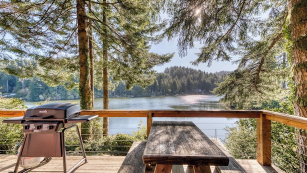 Terraza de madera con una parrilla y una mesa de picnic con vistas a un lago.