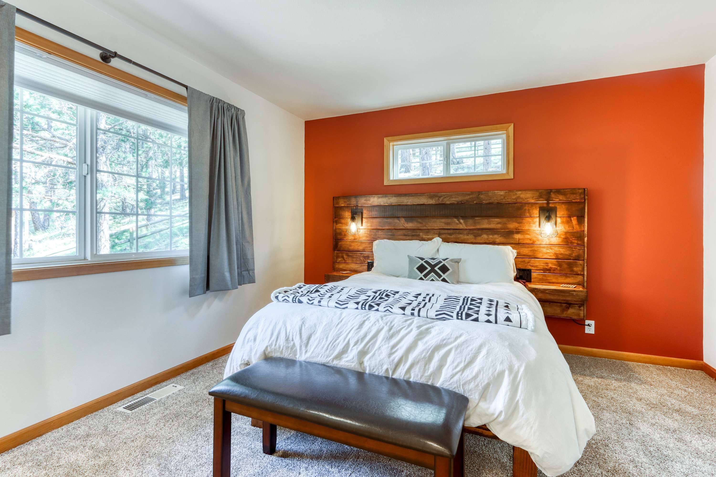 A bedroom with a large window, a wooden headboard, a bed with patterned bedding, and a bench.