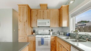 A kitchen with wooden cabinets, a white stove, a microwave, and a large window. - Newer home 1 block from the beach & Prom with fireplace & deck - 2 dogs OK (Seaside)