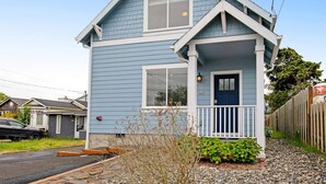 A two-story house with a front porch, a visible garage door, and a small front yard with gravel and plants. - Newer home 1 block from the beach & Prom with fireplace & deck - 2 dogs OK (Seaside)