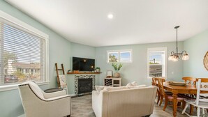 A living room with a fireplace, TV, dining table, and chairs. - Newer home 1 block from the beach & Prom with fireplace & deck - 2 dogs OK (Seaside)