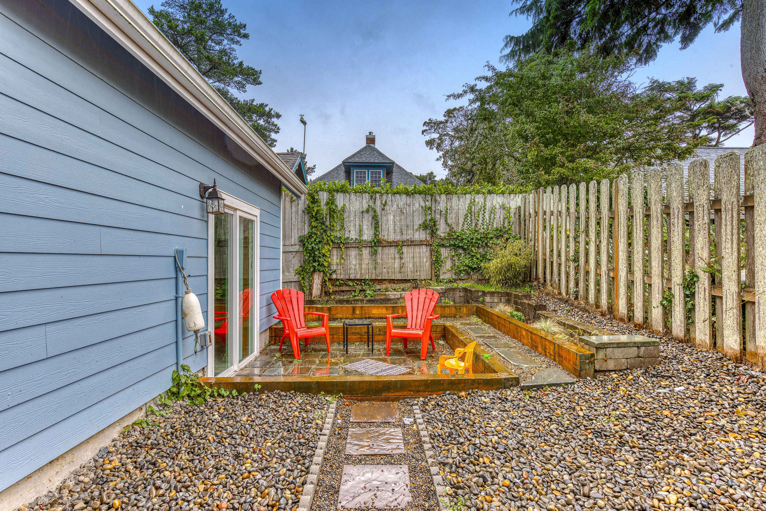 A patio with a wooden fence, a small table, two red chairs, and a yellow toy car. - Newer home 1 block from the beach & Prom with fireplace & deck - 2 dogs OK (Seaside)