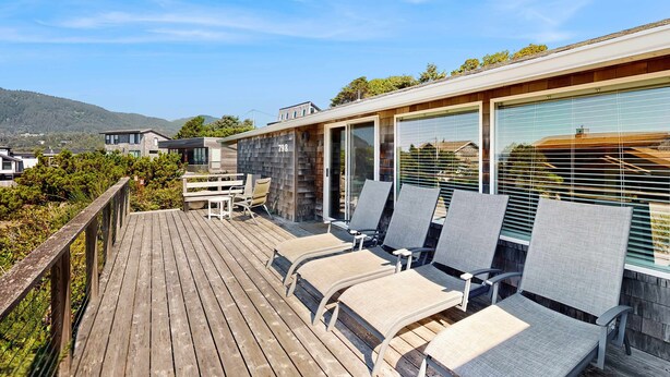 Een houten terras met ligstoelen, een glazen deur en uitzicht op een berg.