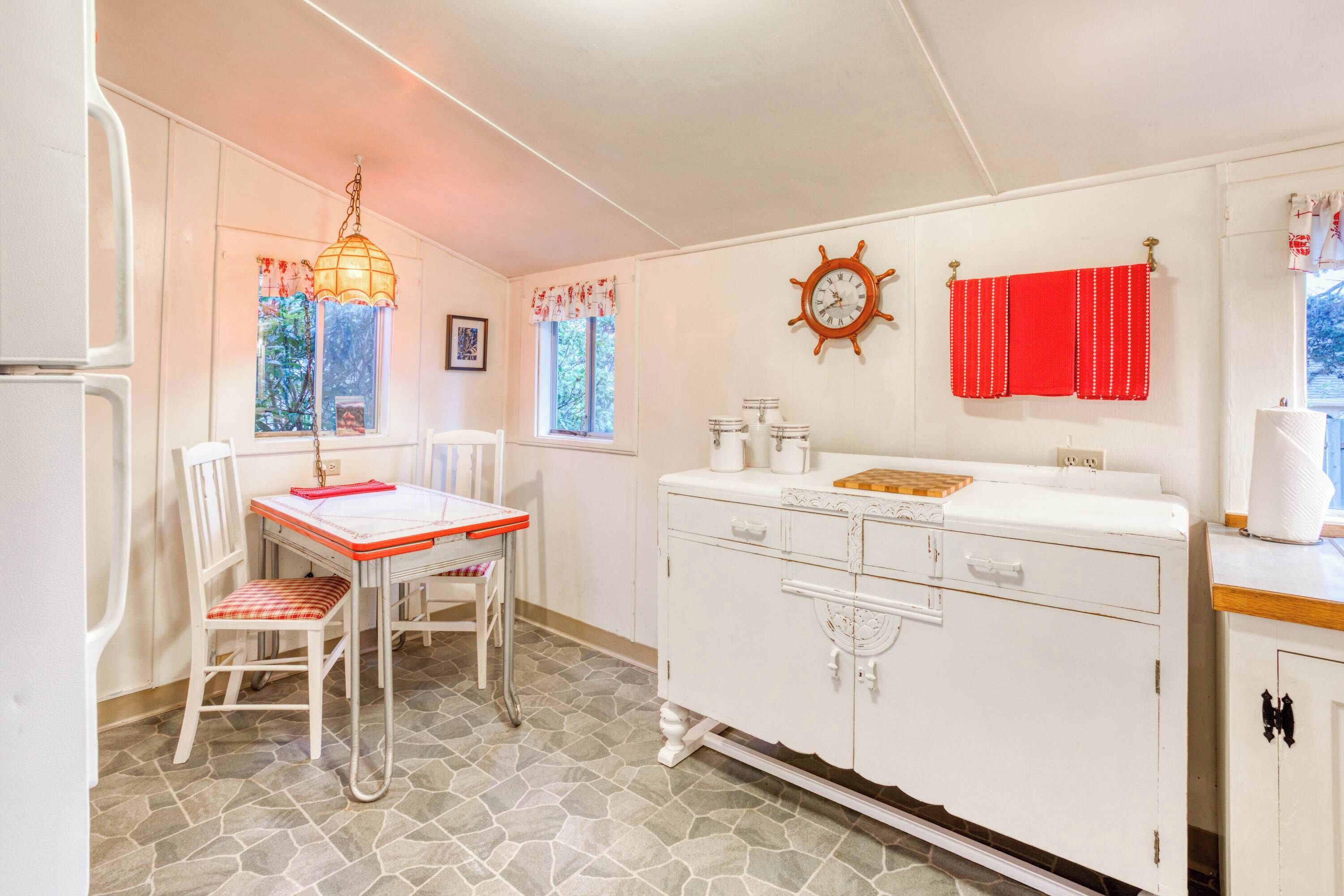Una cocina con piso de piedra, armarios blancos, una mesa de madera y una lámpara colgante.