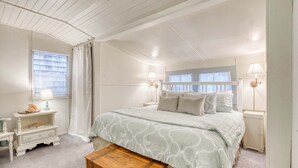 Een slaapkamer met een groot bed, twee nachtkastjes, een nachtkastje, een houten kist en een raam met gordijnen.