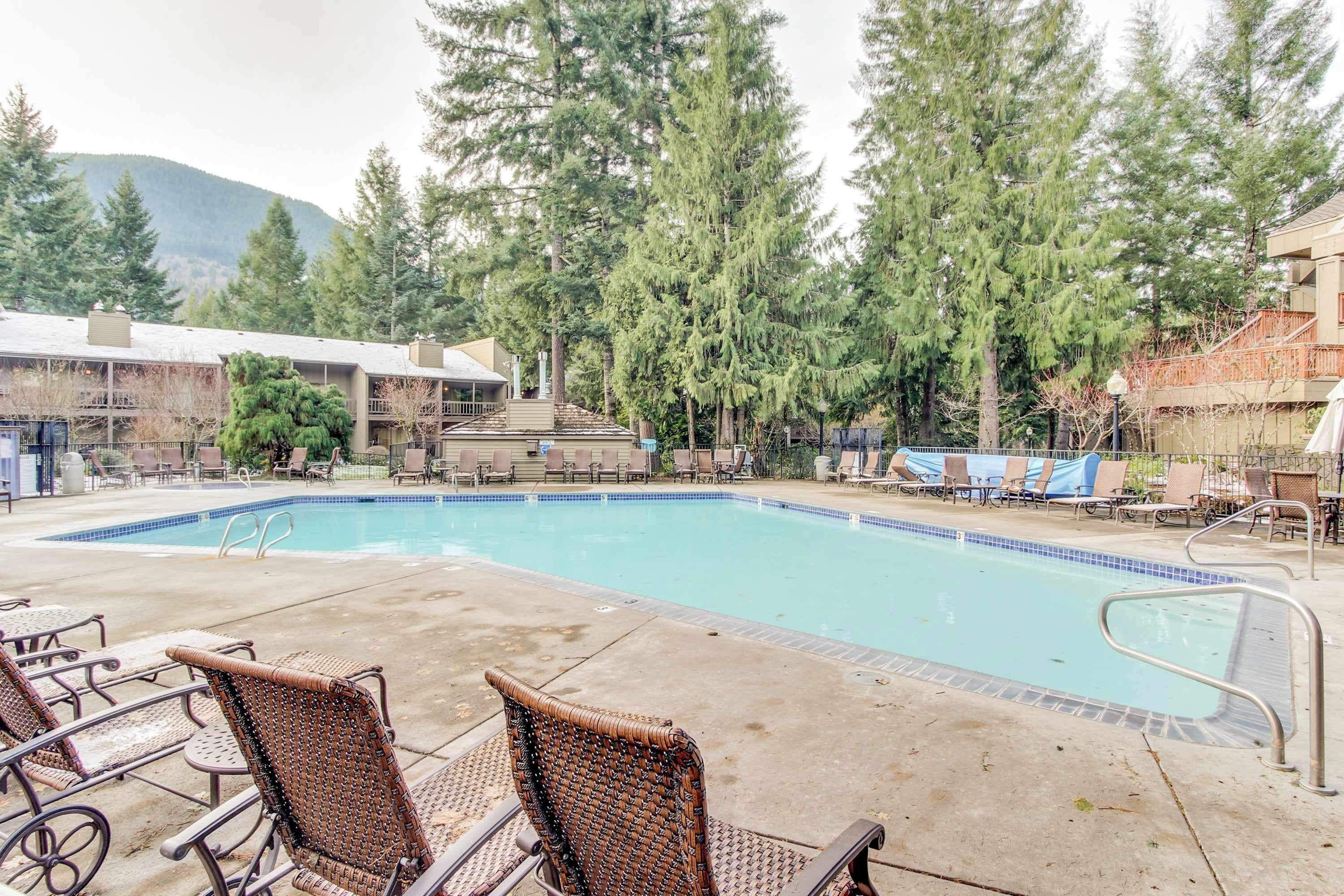 A swimming pool with lounge chairs, surrounded by trees and buildings.