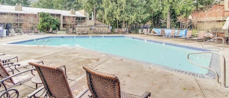 A swimming pool with lounge chairs, surrounded by trees and buildings.