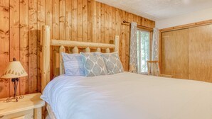Een kamer met houten lambrisering, een bed, een nachtkastje en een raam met gordijnen.