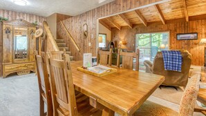 Een houten interieur met een eettafel, stoelen, een bank en een trap.