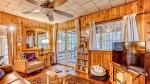 Un interior de madera con ventilador de techo, un sofá, una mesa de centro, una estantería y un televisor.