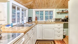 Una cocina con techo de madera, armarios blancos, un lavamanos doble y una ventana con vista a árboles.