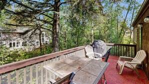 Une terrasse extérieure couverte, dotée d’une table et de chaises, entourée d’arbres et offrant une vue sur une maison.