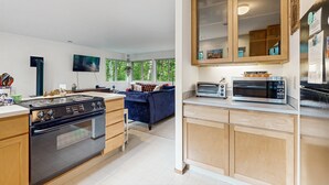 Une cuisine moderne équipée d’une cuisinière, d’un four à micro-ondes et de placards, un coin repas avec une table et des chaises, et un salon avec un canapé et un téléviseur.