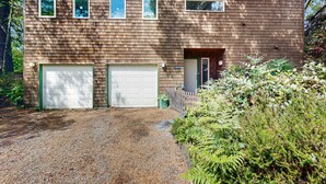 Un bâtiment à deux étages avec un garage, un petit porche et une allée gravillonnée.